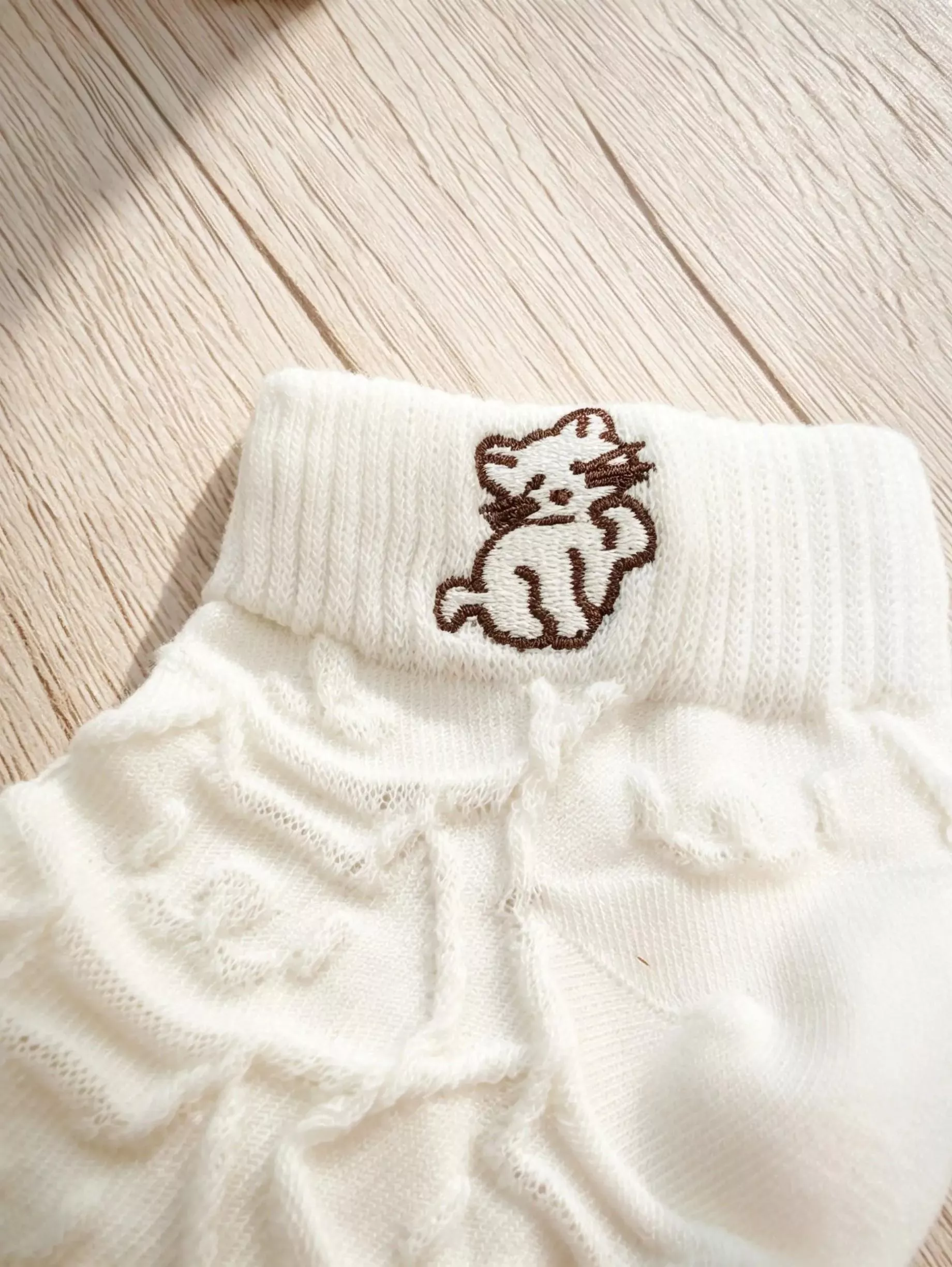 白色針織襪特寫照，清晰呈現襪口的棕色小貓刺繡與下方獨特的立體針織紋路。