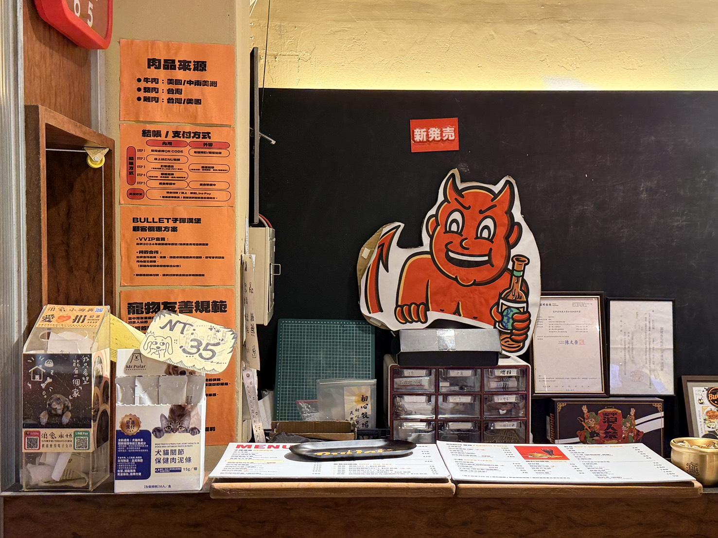 台中西區子彈漢堡(Bullet Burger)櫃檯一景,展示紅色惡魔品牌Logo、菜單與寵物友善規範公告和北極先生寵物食品,呈現餐廳的美式搖滾風格與友善氛圍