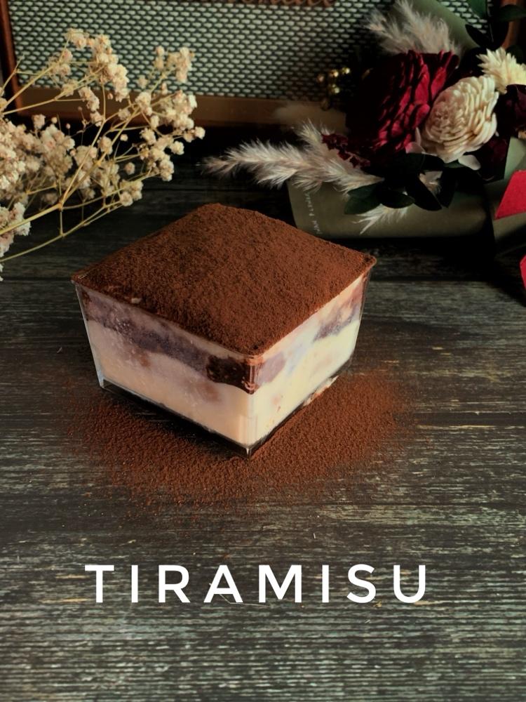方型透明盒裝的傳統提拉米蘇，上層覆蓋厚實的可可粉，並可清楚看