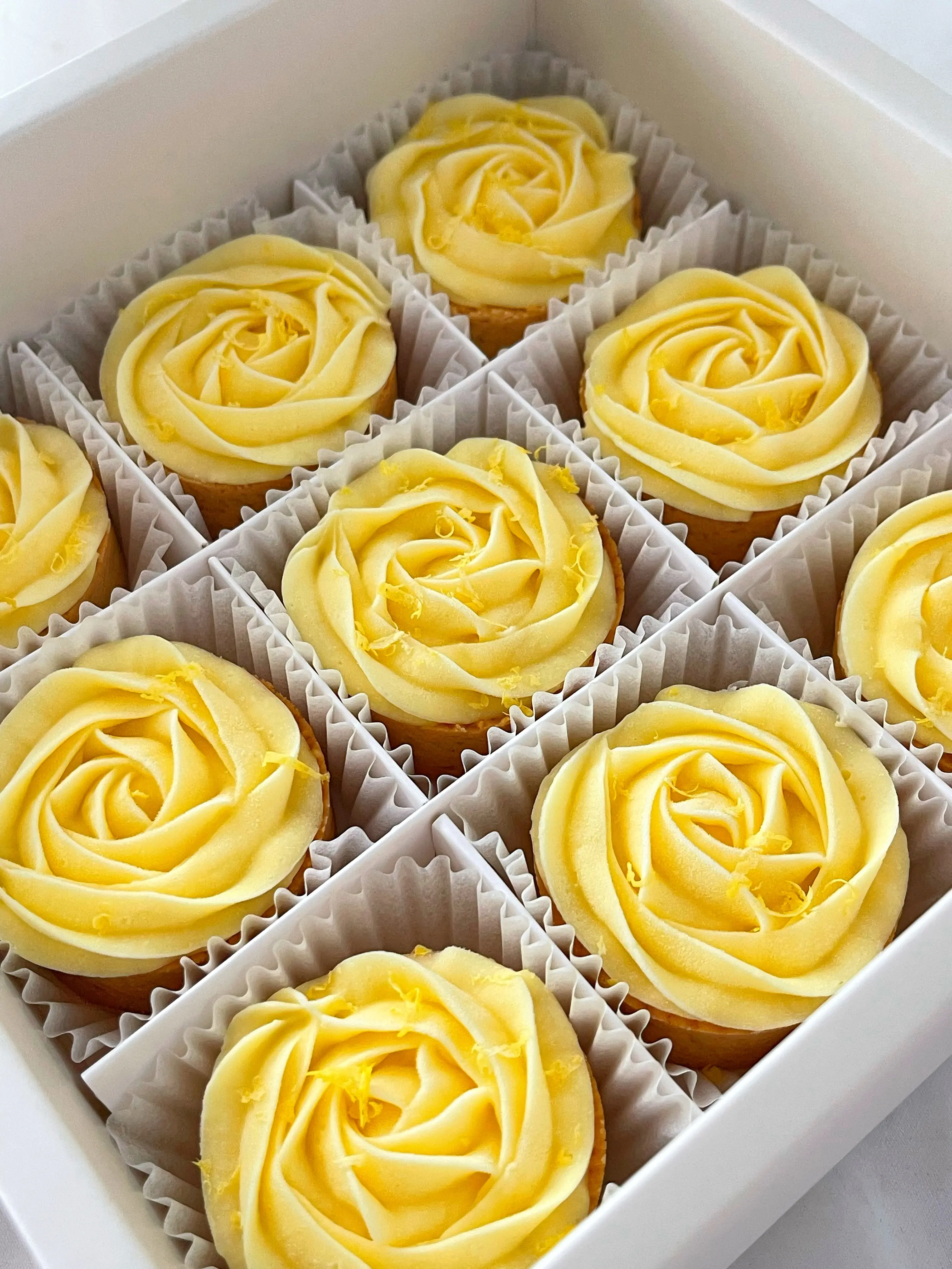 黃色玫瑰奶油霜近拍，花瓣層次分明，中心帶深黃漩渦，表面點綴金黃檸檬皮碎屑，口感柔和酸香