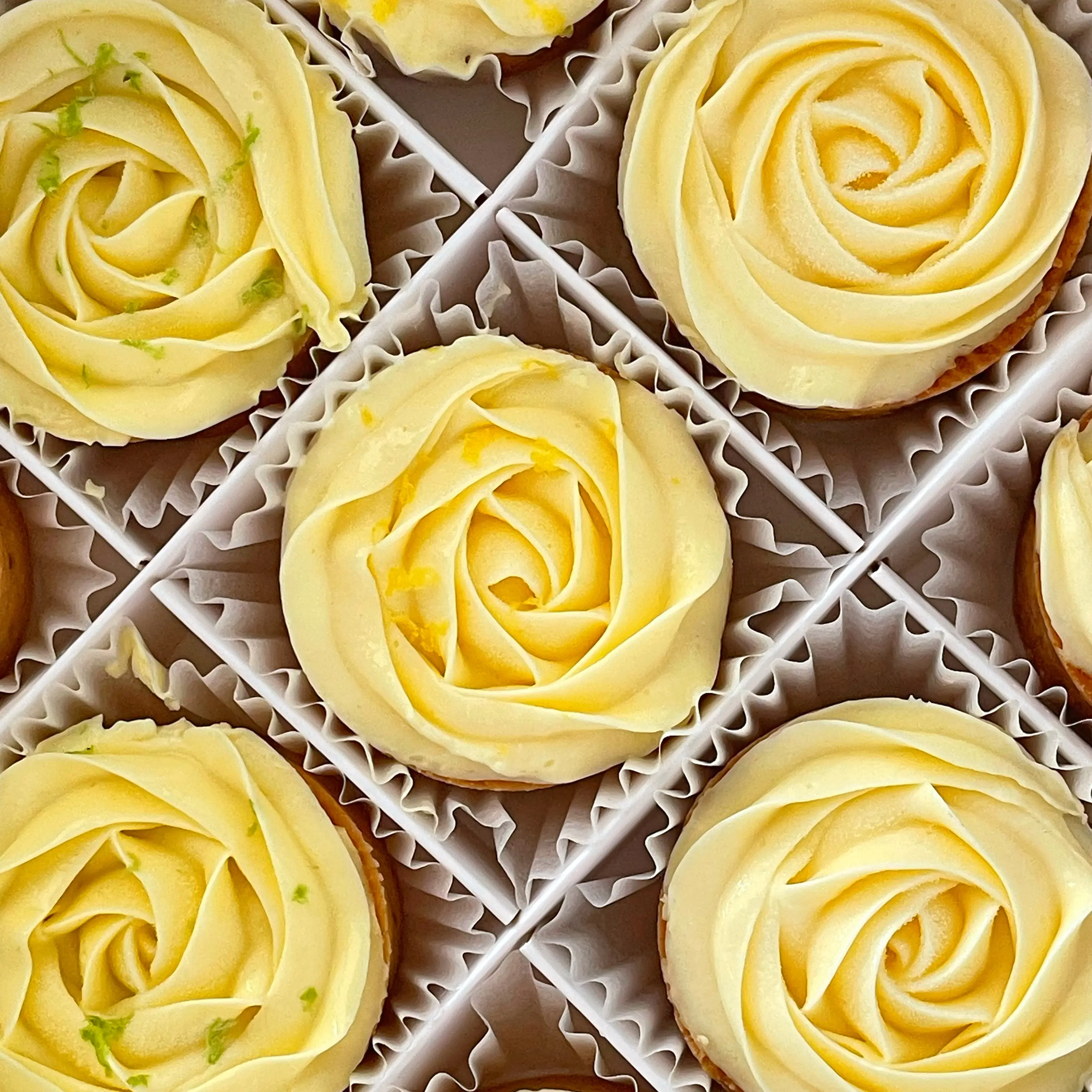 白色禮盒俯視，九顆淡黃色玫瑰塔整齊排列，部分表面點綴橘黃檸檬皮，為經典綠檸檬、柔光黃檸、柚香三種口味組合，台中檸檬塔禮盒