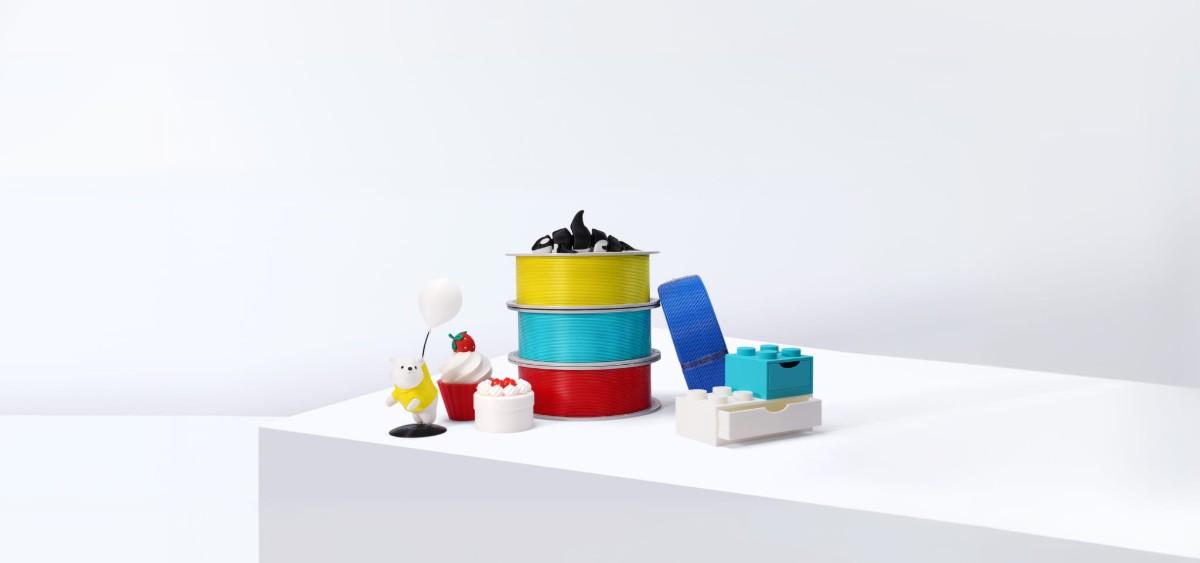 以 Bambu PLA Basic 基礎色系列線材 多色列印的堆疊容器與小物擺在白色平台上（Bambu Lab 原廠圖）